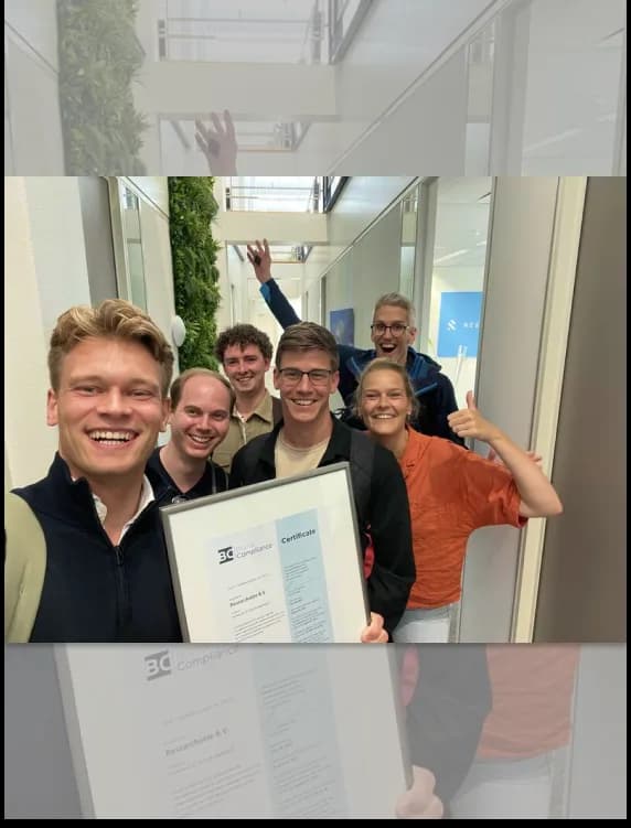 Lachend Researchable-team in de kantoorgang viert de ISO 27001-certificering met het ingelijste certificaat